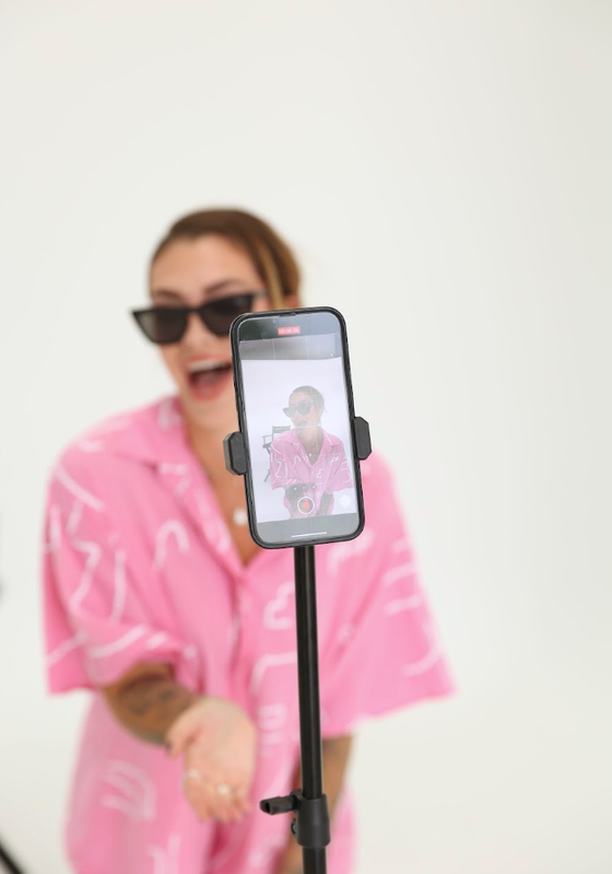 Creator in a pink set filming a piece to camera on a phone